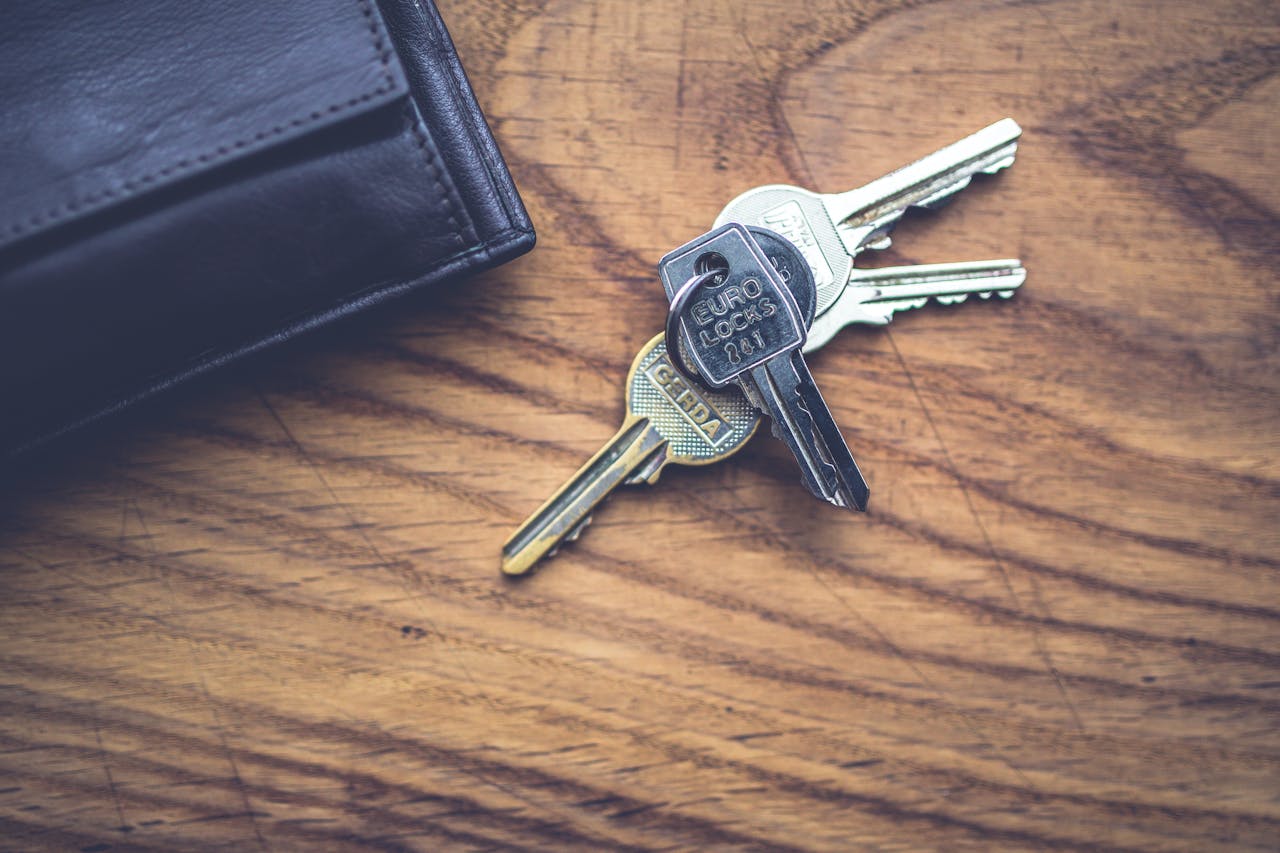 Black wallet and metal keys resting on a textured wooden table.