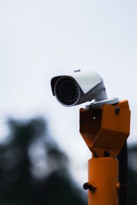 A security camera mounted on an orange stand against a blue sky.