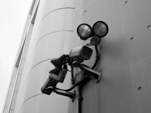 Close-up of a black and white CCTV surveillance camera with spotlights mounted on a building wall.